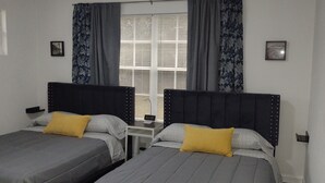 A bedroom with two beds, a nightstand, a window with curtains, and a wall-mounted picture. - Deco style spacious remodeled house in the heart of Sebring close to everything. (Sebring)