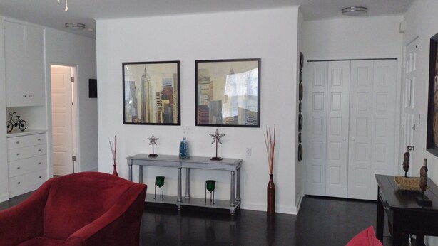 A modern living room with a red armchair, a white console table with decorative items, and two framed cityscape paintings on the wall. - Deco style spacious remodeled house in the heart of Sebring close to everything. (Sebring)