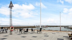 A seaside terrace with tables and chairs, a lifebuoy, and a pier in the background. - 6 Person Holiday Home in Thyholm (Thyholm)