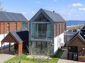 A modern residential building with a large glass balcony, a covered porch, and a view of the sea.
