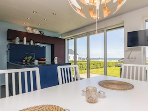 A modern kitchen with a large window, a dining area with white chairs, and a view of the sea. - 6 Person Holiday Home in Thyholm (Thyholm)