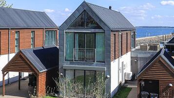A modern residential building with a large glass balcony, a covered porch, and a view of the sea.