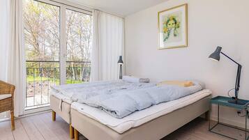A bedroom with a large bed, a desk, a chair, a window with curtains, and a painting on the wall.