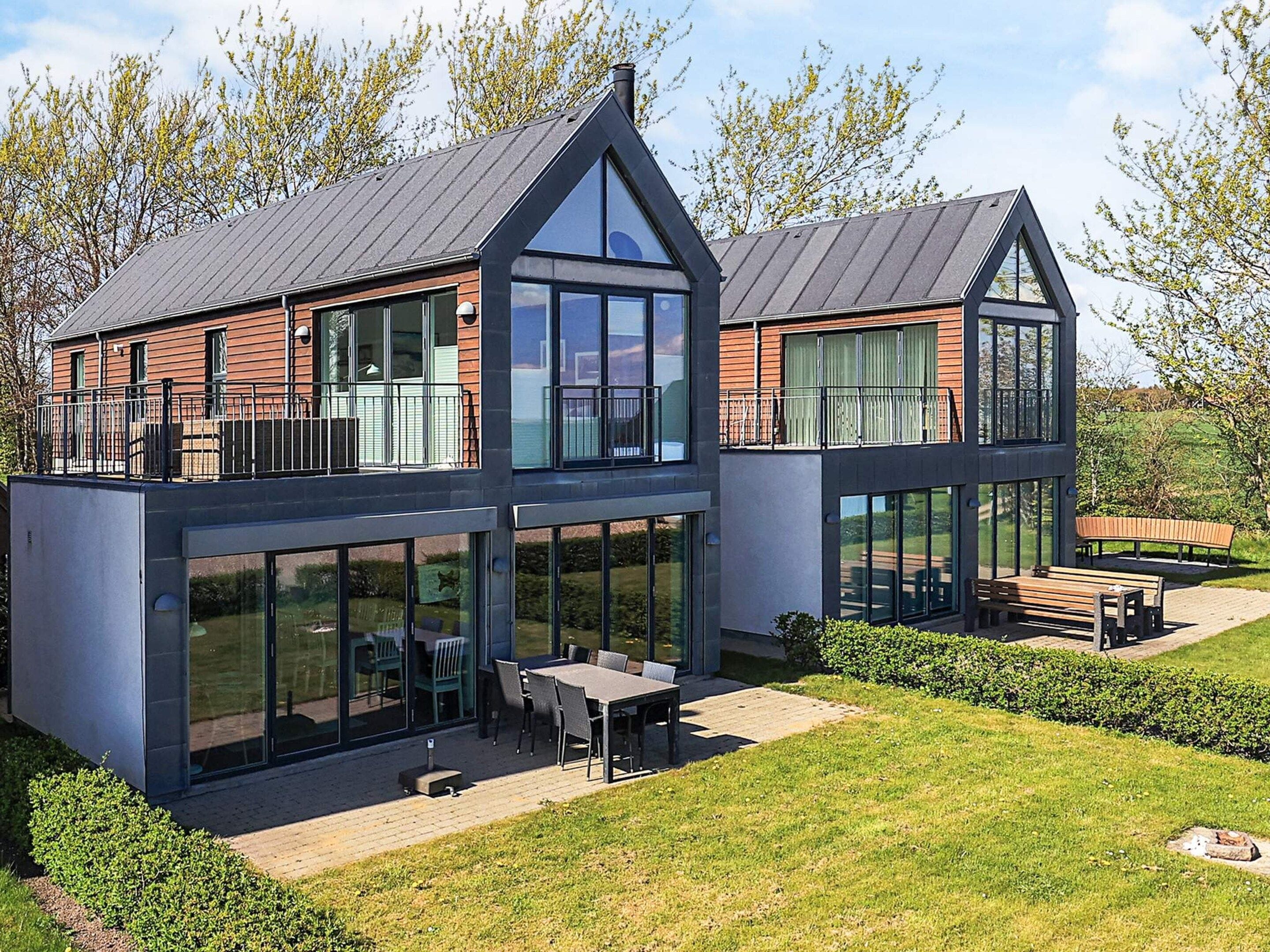 A modern two-story house with large windows, a balcony, and a patio area with outdoor furniture.