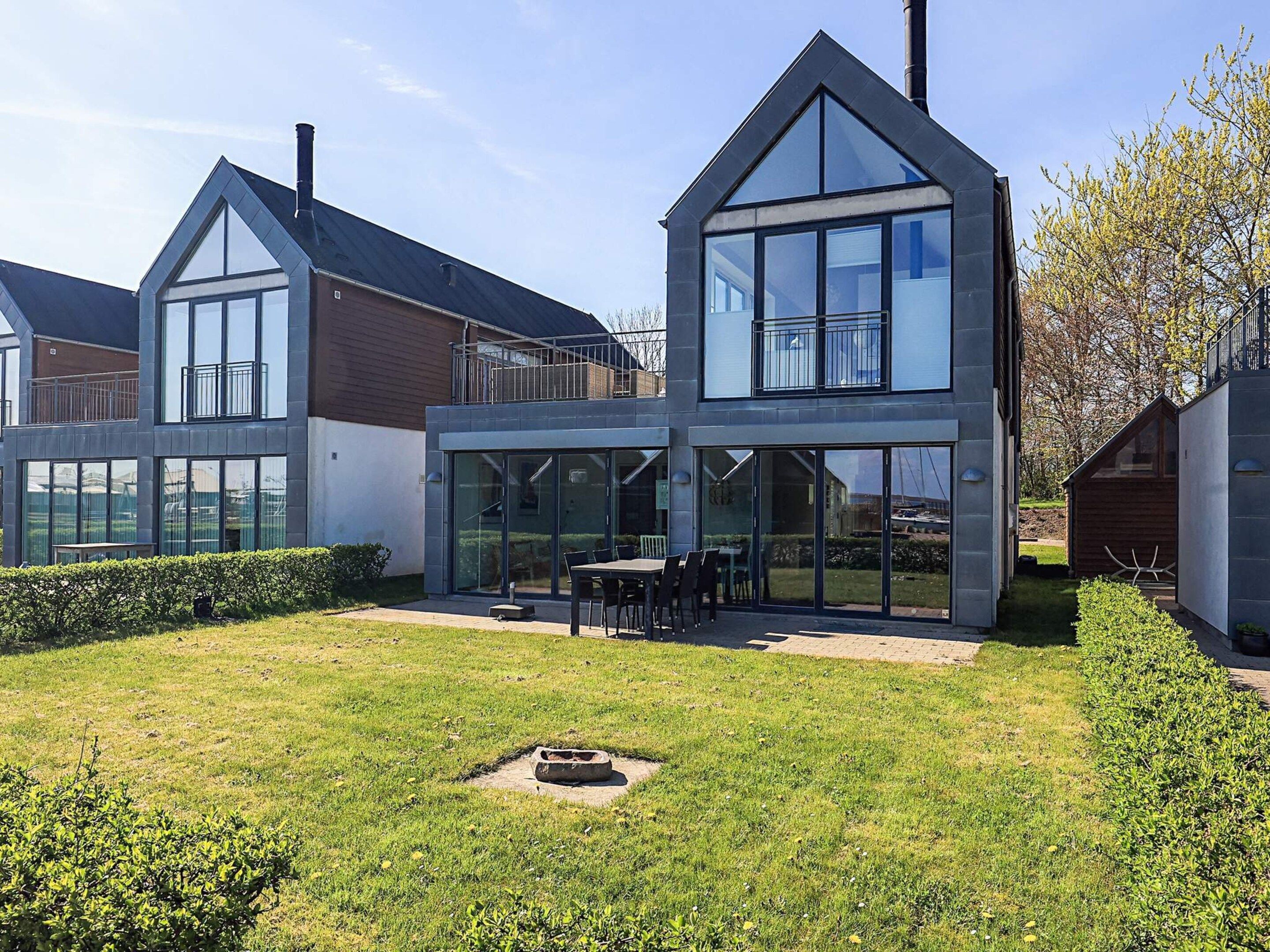 A modern two-story house with large windows, a patio with outdoor furniture, and a well-maintained lawn.