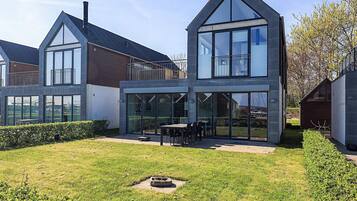 A modern two-story house with large windows, a patio with outdoor furniture, and a well-maintained lawn.