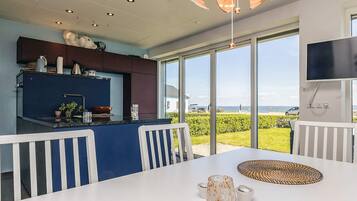 A modern kitchen with a large island, a dining area with white chairs, and a view of the sea through large windows.