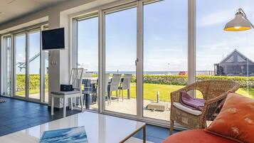 A modern room with large windows, a flat-screen TV, a sofa, and a dining area with chairs.