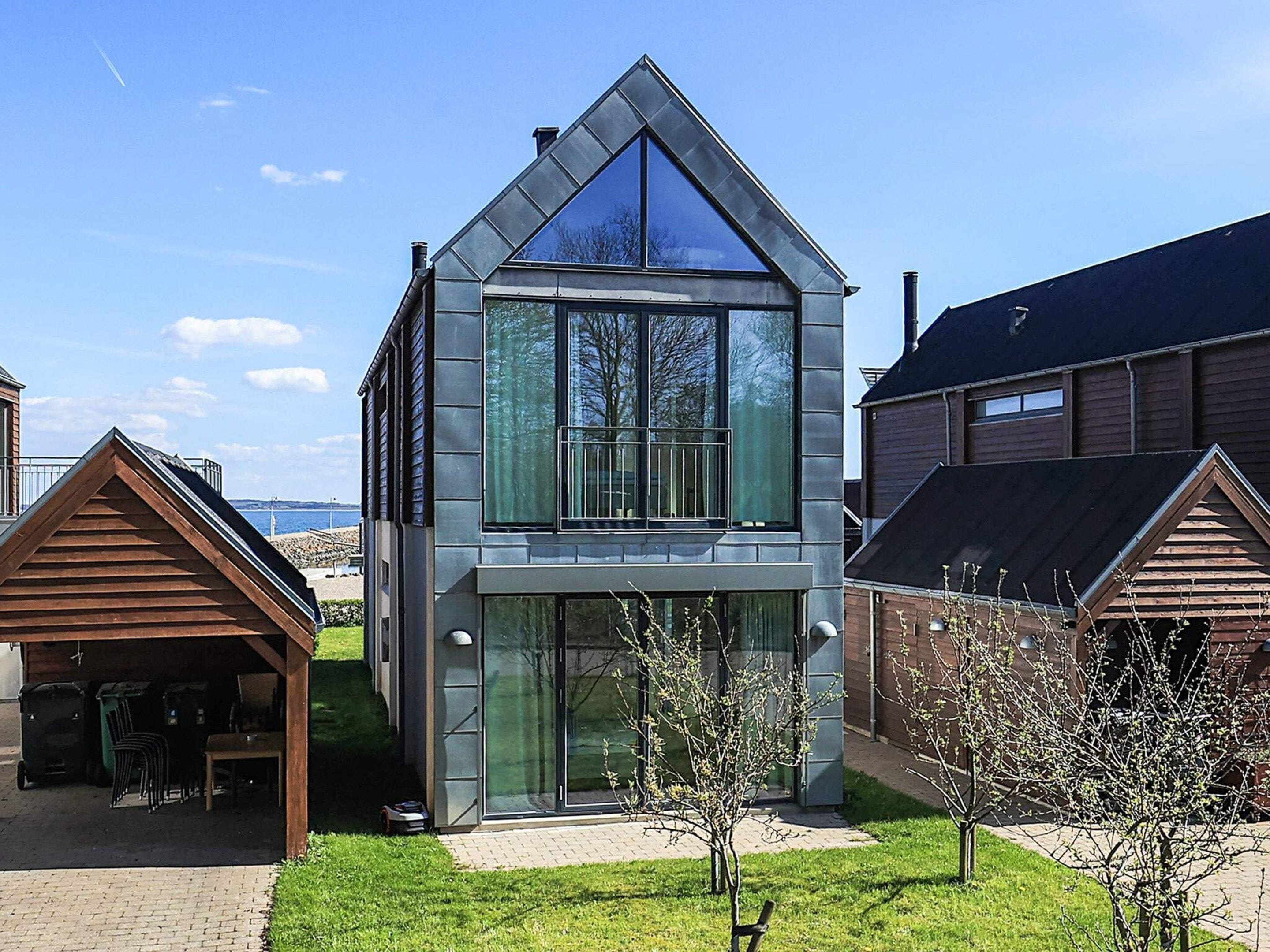 Une maison moderne à deux étages, dotée d’une grande baie vitrée, d’un toit en pente et d’un petit porche.