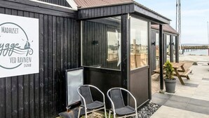 A small, modern outdoor seating area with two chairs and a table, a sign with text, and a view of the water. - 6 Person Holiday Home in Thyholm (Thyholm)