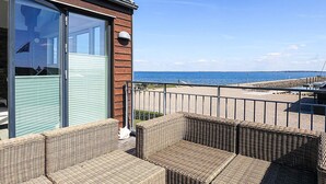 A coastal building with a balcony, wicker furniture, and a view of the sea. - 6 Person Holiday Home in Thyholm (Thyholm)