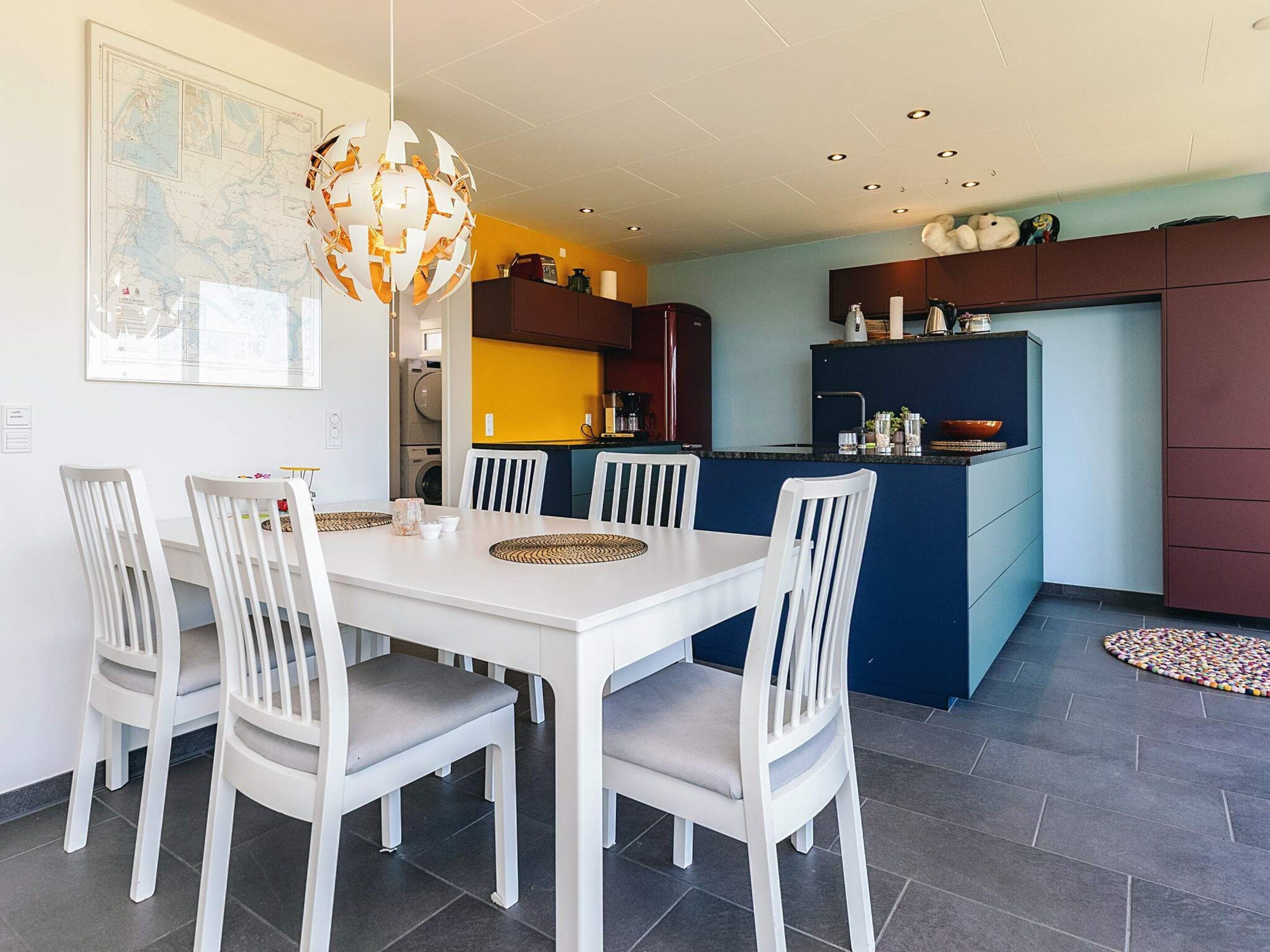 Une cuisine moderne avec un coin repas, comprenant une table à manger blanche avec des chaises, un luminaire sphérique original et une carte accrochée au mur.