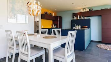 Une cuisine moderne avec un coin repas, comprenant une table à manger blanche avec des chaises, un luminaire sphérique original et une carte accrochée au mur.