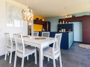 A modern kitchen with a dining area, featuring a white dining table with chairs, a unique spherical light fixture, and a map on the wall.