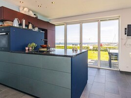 A modern kitchen with a large island, built-in appliances, and a view of the sea through large windows.