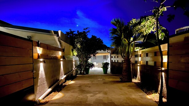 A nighttime view of a gated driveway leading to a building with a visible garage door. - Ti Case Fleur Letchi - Cadre Calme et Agréable, Avec Jardin (Les Avirons)