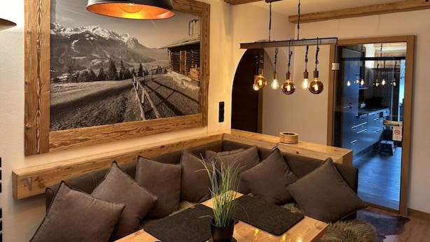 A modern living room with a large framed photograph on the wall, a wooden bench with cushions, and a hanging light fixture.