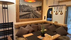 A cozy dining area with a wooden table, cushioned seating, a framed landscape photo, and pendant lighting.