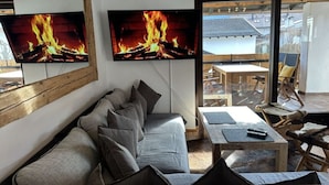 A cozy room with a sofa, a table, and a TV displaying a fireplace.