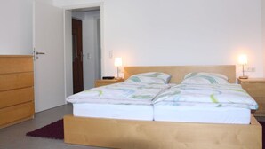 Una camera da letto con un letto in legno, due comodini con lampade, un'armadio in legno e una porta che dà su un'altra stanza.