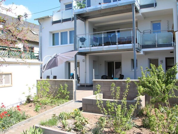 A two-story residential building with a balcony, outdoor seating, and a garden area.