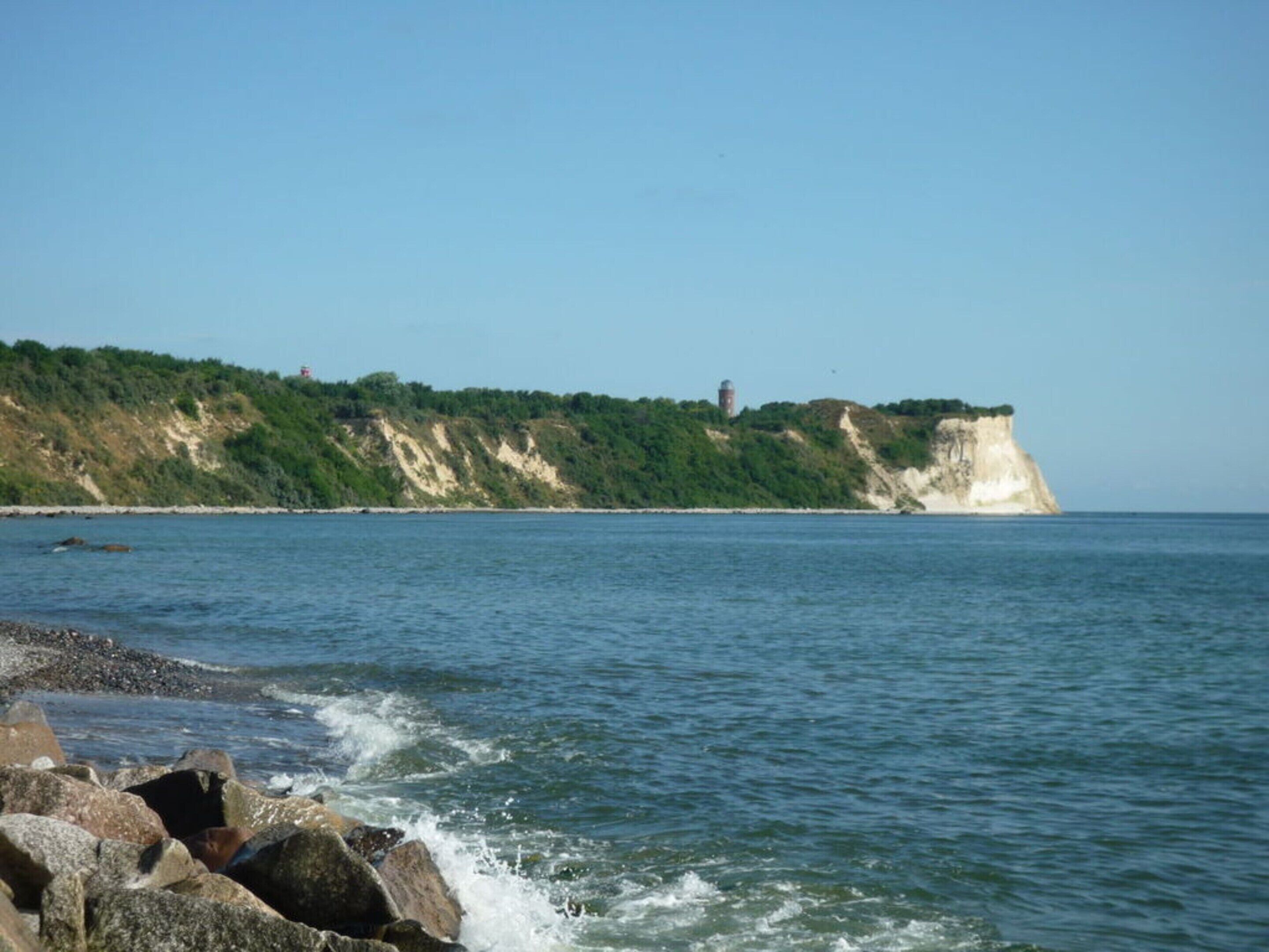 A coastal scene with a rocky shoreline, cliffs, and a lighthouse.