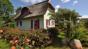 A quaint house with a thatched roof, surrounded by lush greenery and vibrant flowers. - Red-throated Diver Modern Retreat (Putgarten)