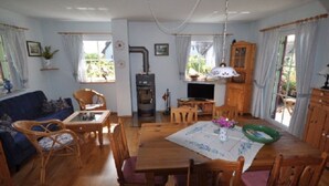 A cozy living room with a sofa, dining table, and chairs, a wood-burning stove, and a television. - Red-throated Diver Modern Retreat (Putgarten)