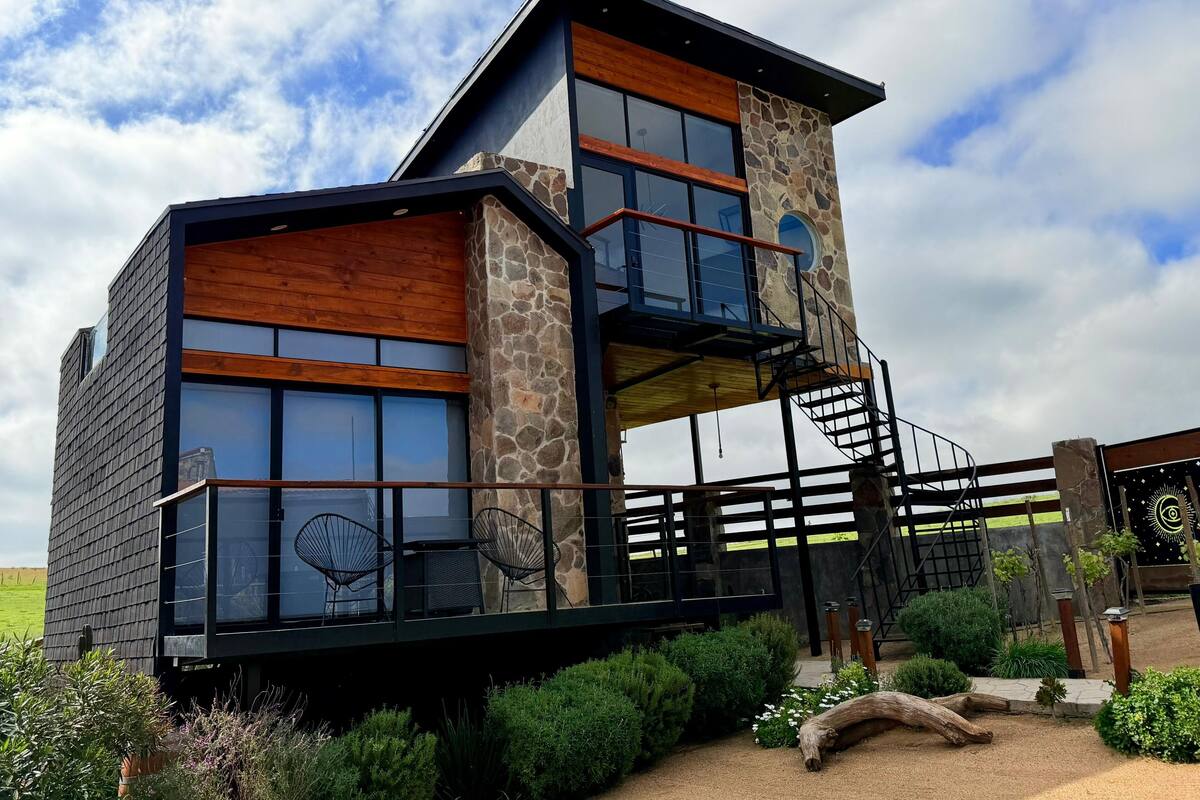 A modern two-story house with a stone facade, large windows, and a wooden deck.