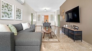 A modern living room with a grey sofa, a coffee table, a TV mounted on the wall, and a dining area in the background. - #3 - Charming Spanish Colonial Apartment - Miramar (San Juan,)