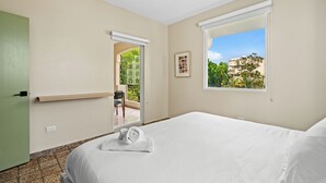 A hotel room with a bed, a window with a view of greenery, a door leading to an outdoor area, and a small table with a chair. - #3 - Charming Spanish Colonial Apartment - Miramar (San Juan,)
