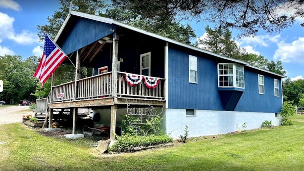 Ein zweistöckiges Haus mit Veranda, einer amerikanischen Flagge und einem Schild mit der Aufschrift 'God Bless the USA'.