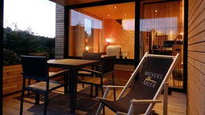 An outdoor seating area with a table and chairs, a lounge chair with "Meyers Beer" branding, and a view of the interior through large glass doors. - Holiday Apartment in Thuringia (Zierow)