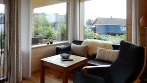 A cozy living room with a wooden ceiling, a large window with curtains, a sofa with cushions, and a small table with a bowl and remote control. - Holiday Apartment in Thuringia (Zierow)