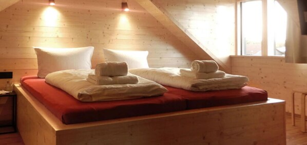 Una habitación acogedora, con paneles de madera, que tiene una cama con ropa de cama roja y toallas impecablemente dobladas.