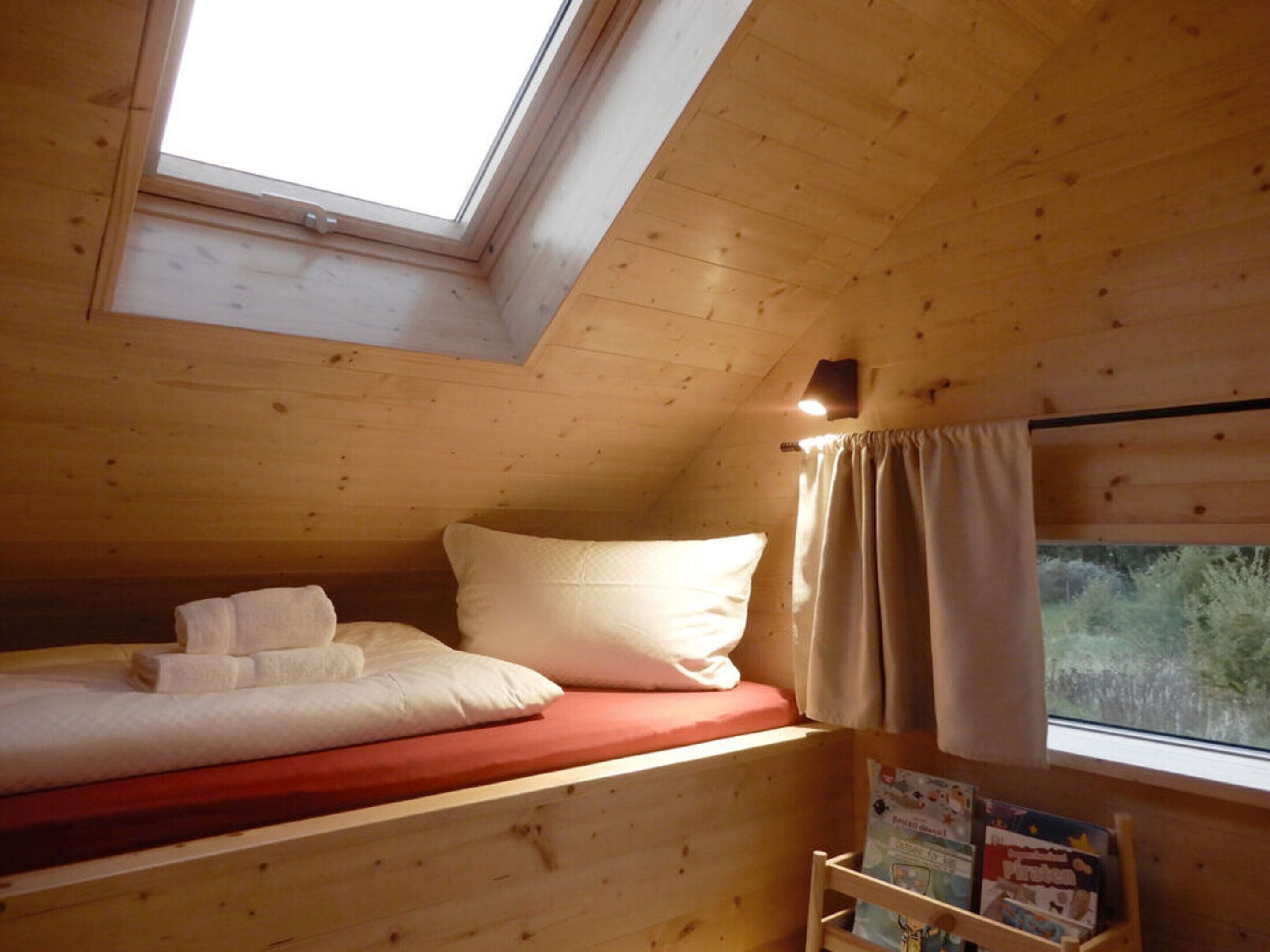 A small, cozy room with a wooden bunk bed, a skylight, and a window with curtains.
