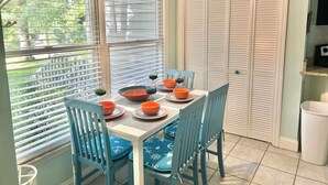 Comedor con una mesa dispuesta para cuatro personas, sillas azules y vistas al exterior.