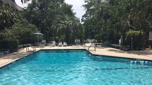 Una piscina cristalina rodeada de sillas de descanso y sombrillas, con un cartel que indica que no hay socorrista de guardia.