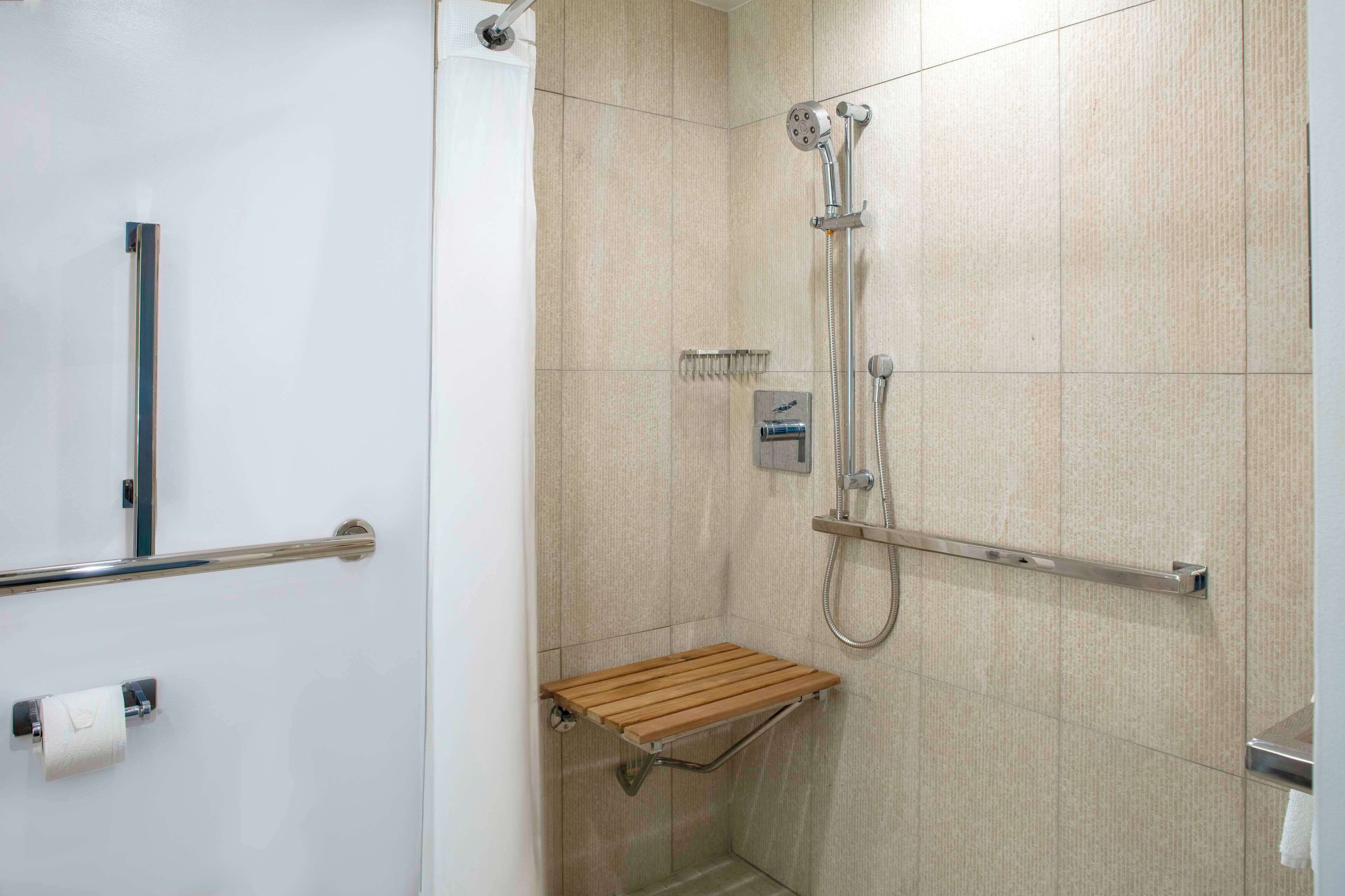 Un baño moderno con ducha, barras de apoyo y un perchero para toallas.