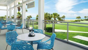 A covered outdoor seating area with tables and chairs, overlooking a grassy area and the ocean. - The Ellie Beach Resort Myrtle Beach, Tapestry By Hilton (Myrtle Beach)