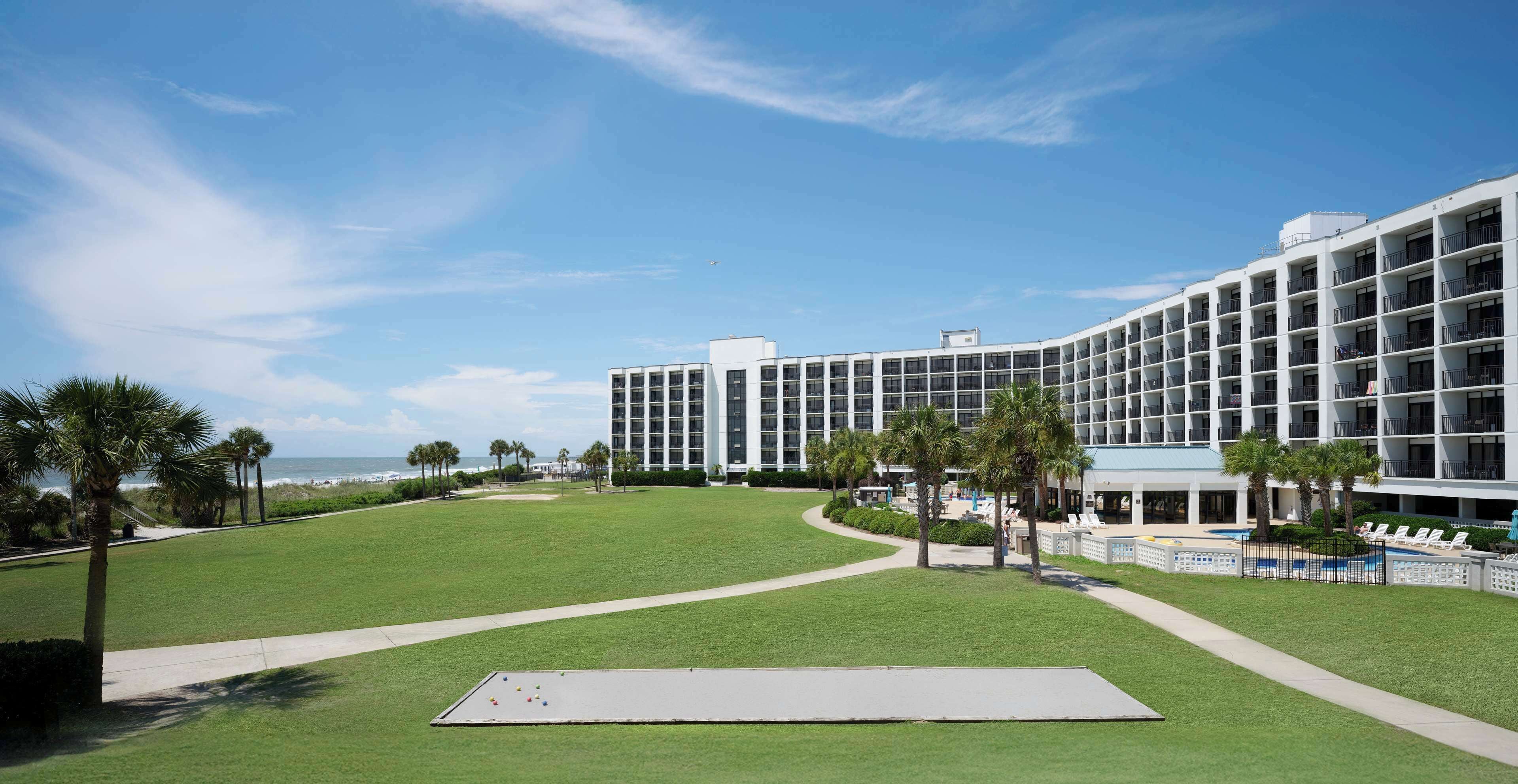 A modern hotel with a large lawn, a pool area, and a view of the ocean.