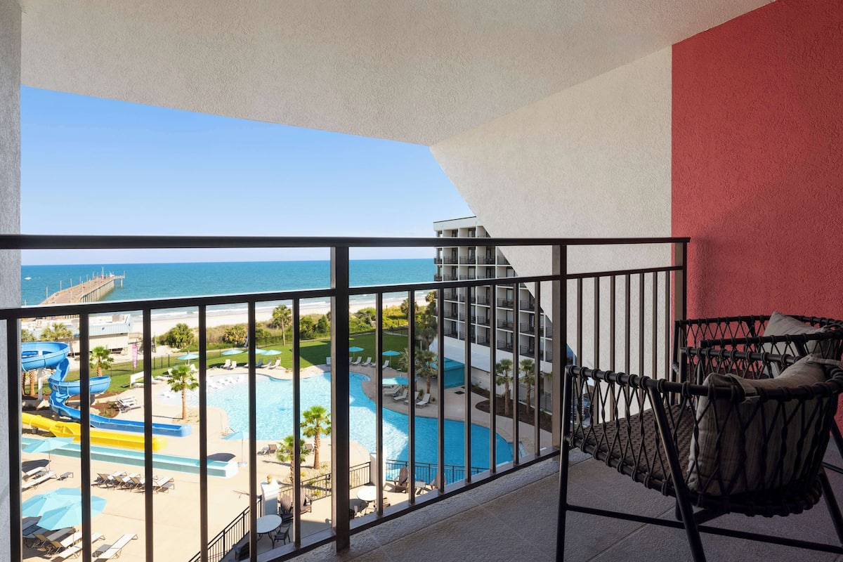 A balcony with a view of a swimming pool and water slides, a red wall, and a black chair.