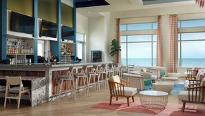 A bar area with a view of the ocean, bar seating, and a large plant. - The Ellie Beach Resort Myrtle Beach, Tapestry By Hilton (Myrtle Beach)