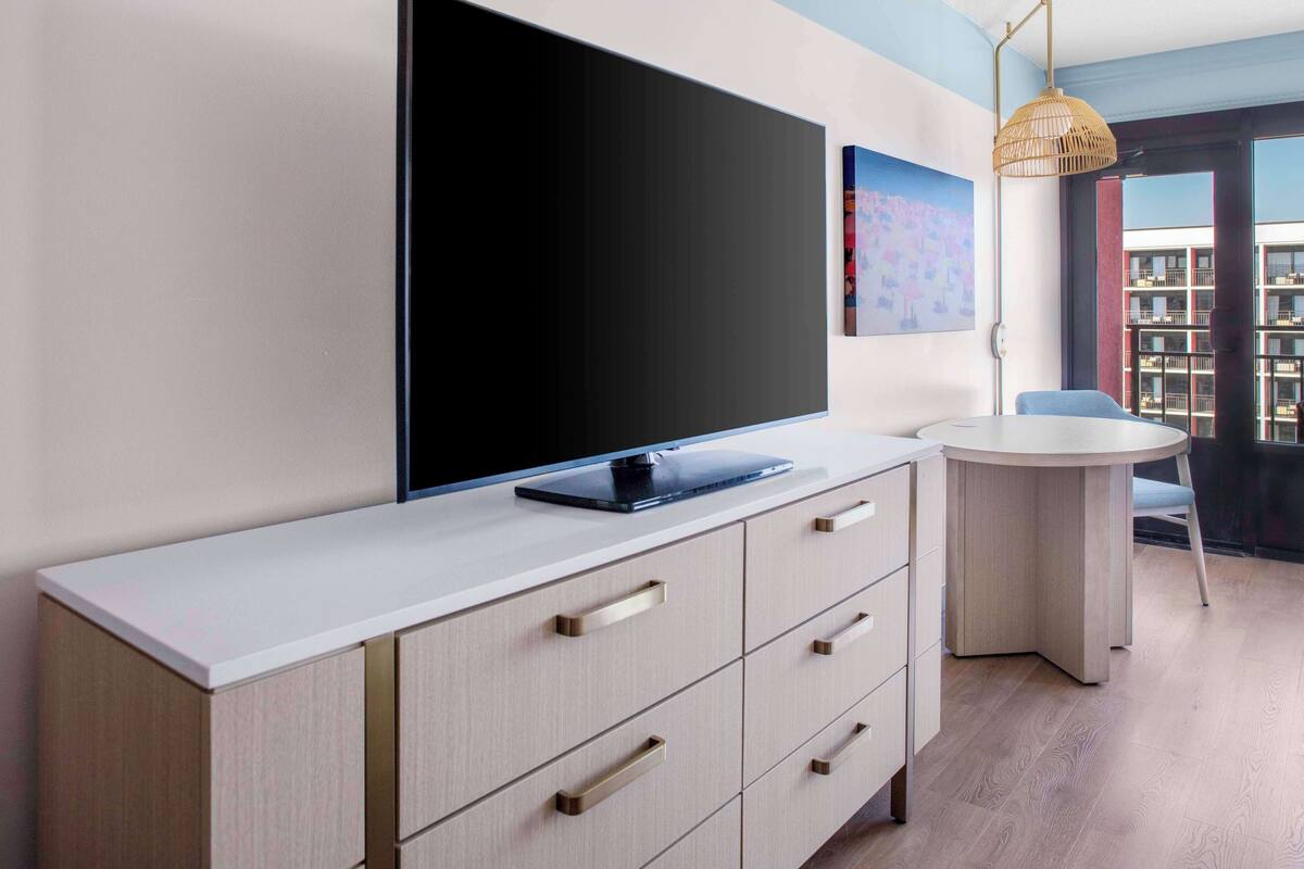 A modern room with a flat-screen TV on a white console, a round table, and a chair.