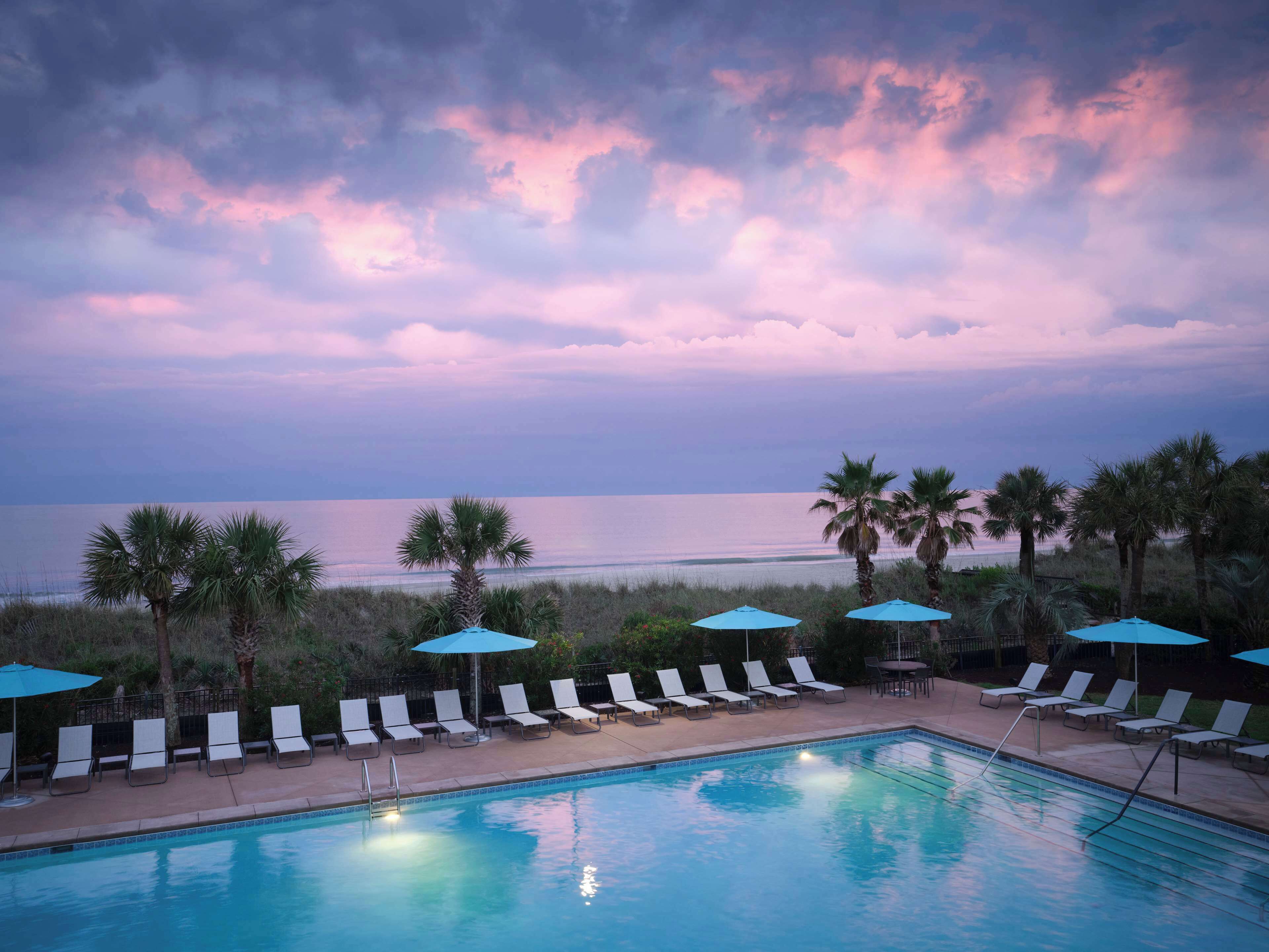 A poolside area with lounge chairs and umbrellas, overlooking a beach and ocean.