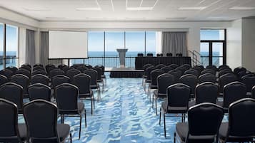 Un salón de conferencias con filas de sillas, un escenario y una pantalla grande.