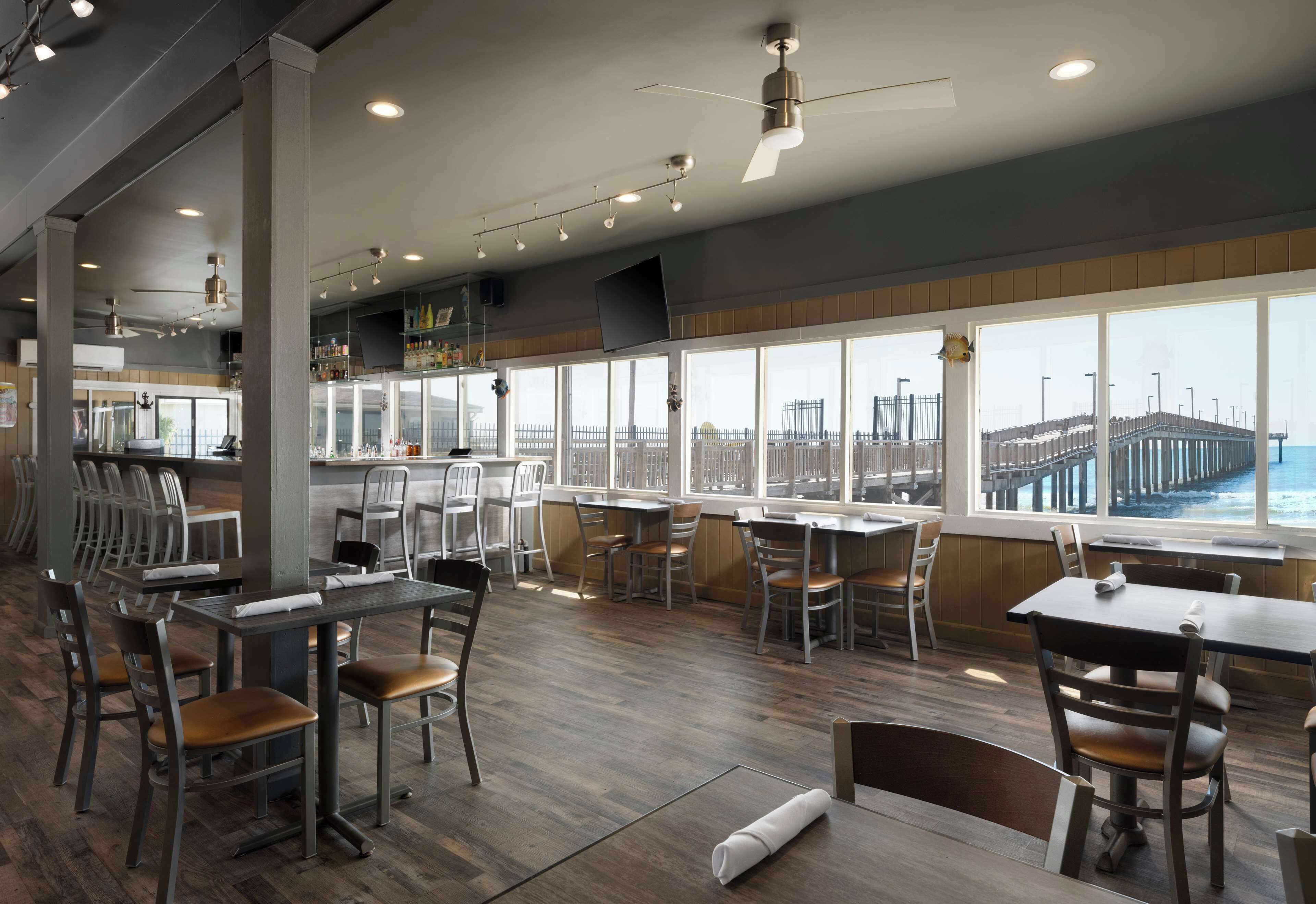 A restaurant with a view of a pier, wooden flooring, and modern furniture.