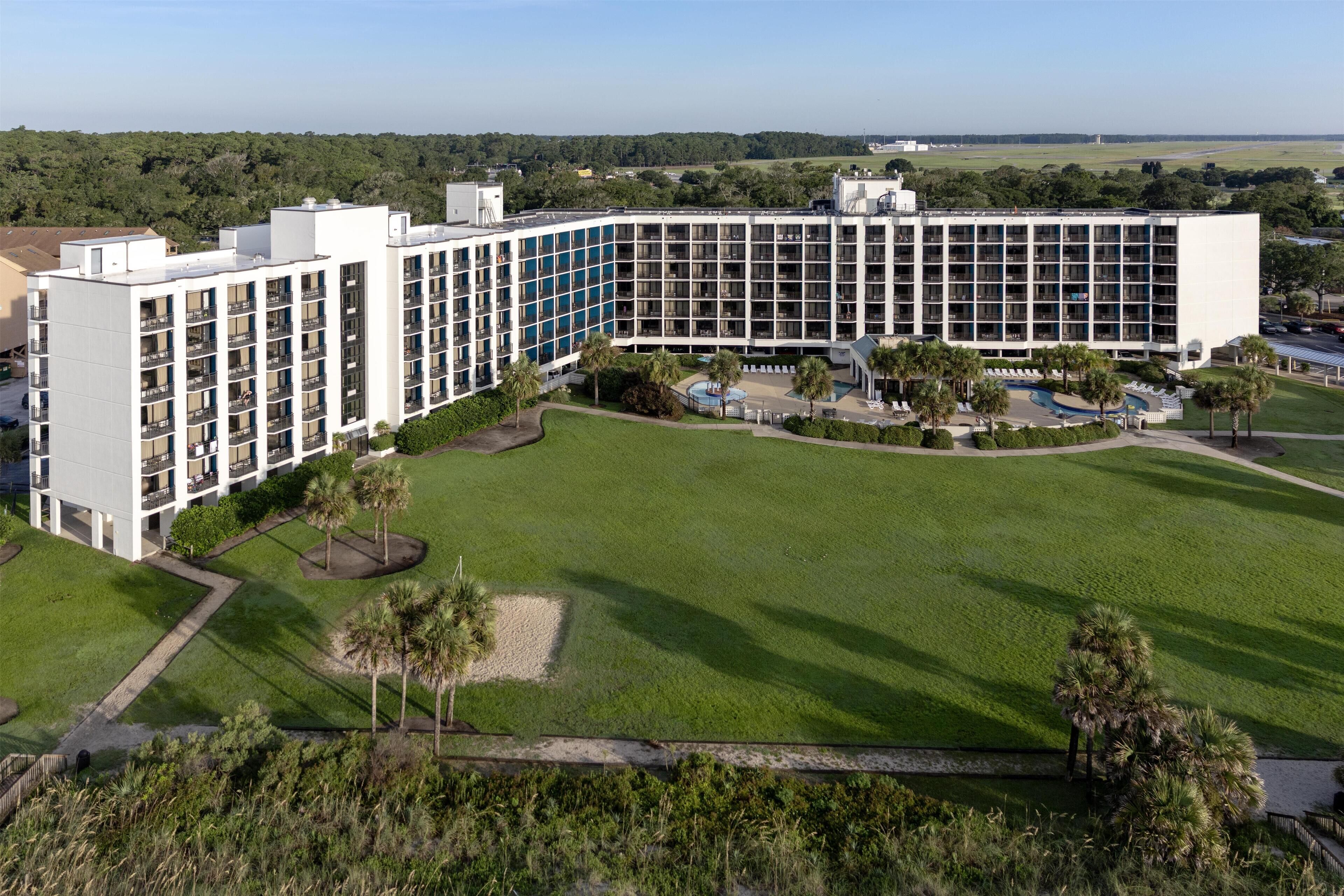 A large hotel with multiple floors, a central courtyard with a swimming pool, and surrounding greenery.