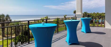 A balcony with blue tables and chairs, overlooking a beach and pool area.