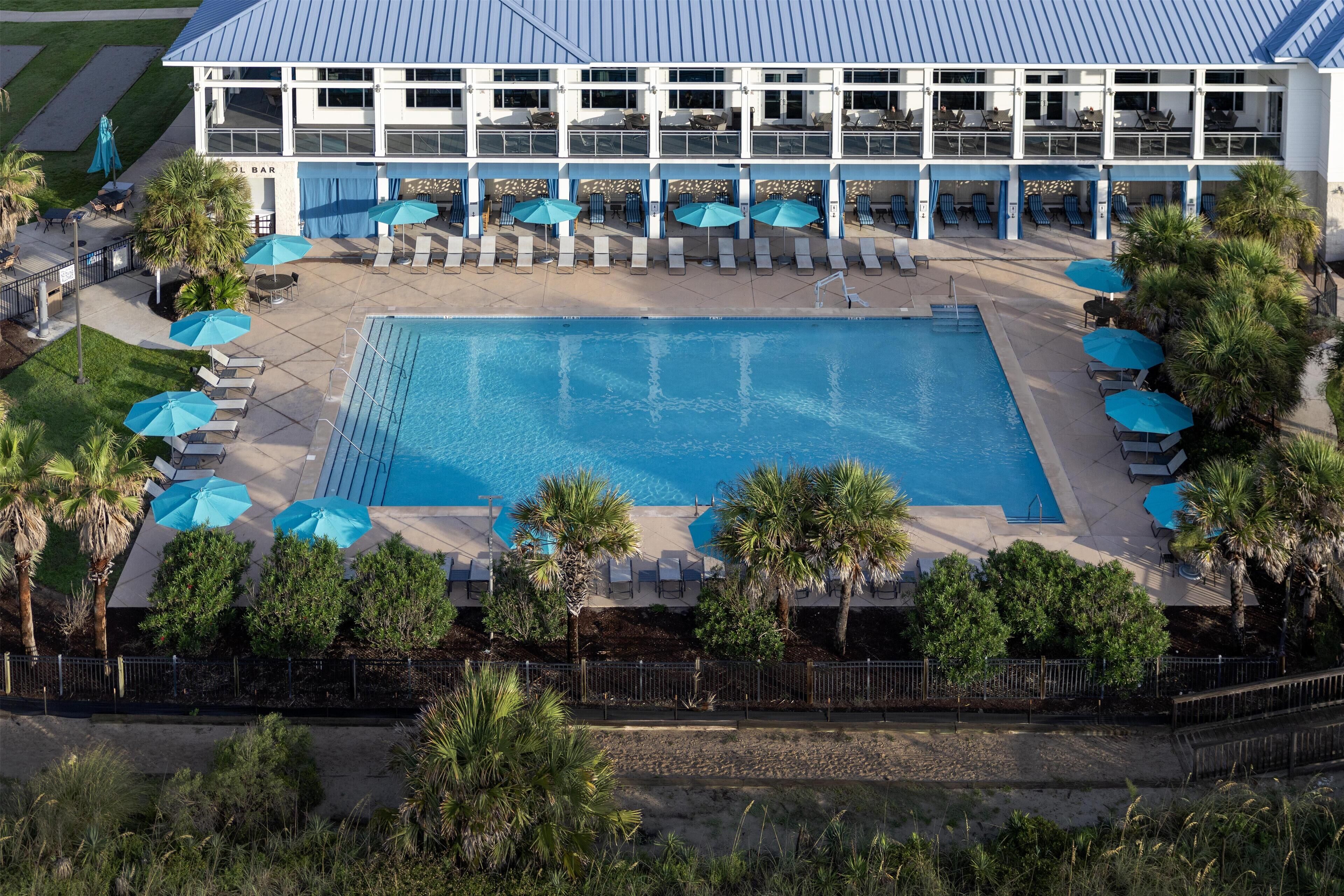 Une grande piscine entourée de chaises longues et de parasols, avec un bâtiment en arrière-plan.